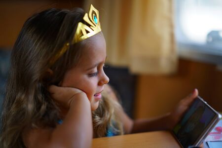 Portrait of 4 year old girl wearing a toy crown and looking at cell phone