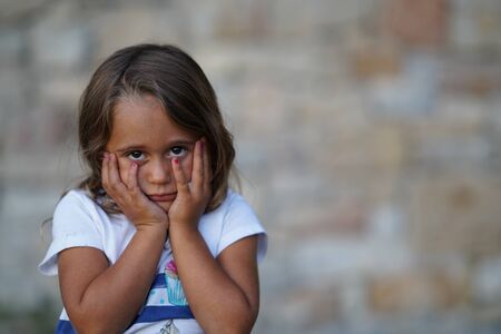 Portrait of a 4-year-old girl with the hands on the face looking straight at the camera with a sade faceの写真素材