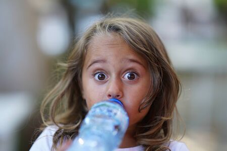 portrait of a very pretty 4 year old girl drinking water from a plastic bottle