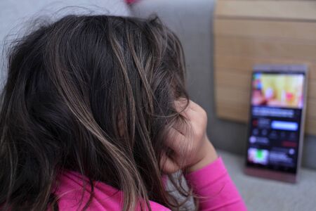 4-5 year old girl looks at the smart phone on the sofa at home