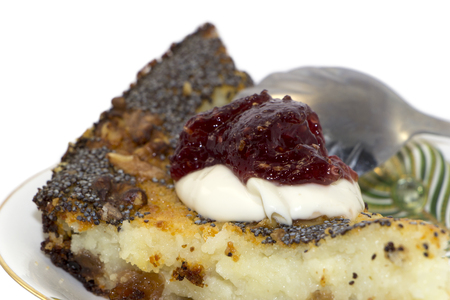Sweet piece of pie with poppy seeds, raisins, cottage cheese and nuts on a saucer. Sour cream, jam and spoon on it. Close up. Isolated on white background.の写真素材