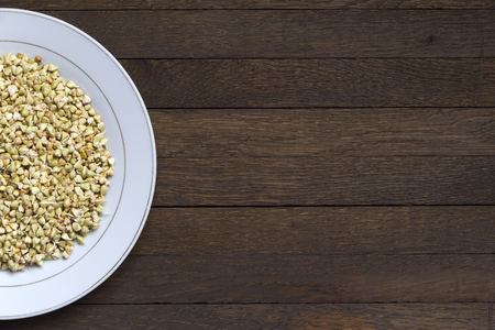 Half of white plate with Sprouted buckwheat inside on wooden table. Close up background with copy space. Top view. Left position. Organic raw hulled groats. Concept of healthy nutrition. Vegan food.の写真素材