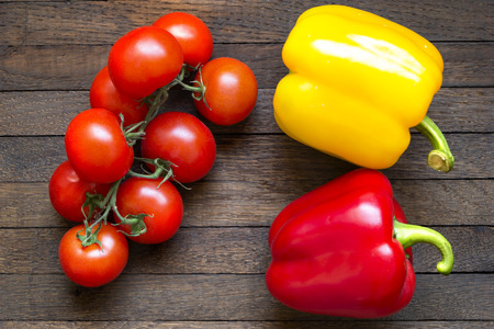 Red and yellow sweet bell peppers and ripe tomatoes on branch on dark wooden table from oak. Top view. Close up. Raw foods background. Healthy nutrition concept.の写真素材