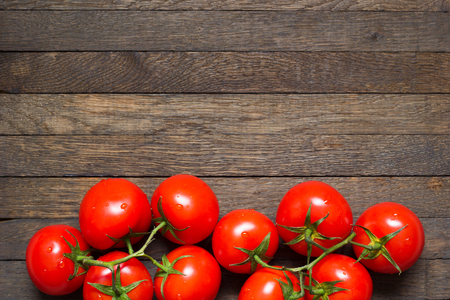 Red washed ripened tomatoes in bottom part of wooden background. Copy space on top. Water droplets on freshness vegetables. Top view. Close up. Healthy nutrition concept. Raw foods. Vegan menu.の写真素材