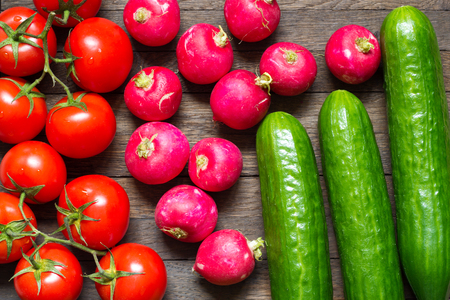 Agriculture background. Tomatoes, radishes and cucumbers on wooden table. Fresh raw food. Water drops on washed vegetables. Close up. Top view.の写真素材