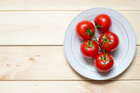 Ripened tomatoes on white plate on light wooden table with copy space. Location at right side. Top view background. Close-up. Washed vegetables on green branch. Healthy meal concept.の写真素材
