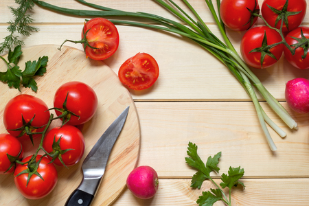 Healthy food cooking concept. Fresh tomatoes on branch, radish, onion, dill and parsley laid out on rustic light wooden table. Knife on kitchen board. Top view. Natural organic ingredients.の写真素材