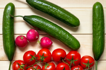Natural food background with cucumbers, tomatoes and radishes. Ripened vegetables laid out on light wooden table. Top view. Close-up. Fresh raw foods.の写真素材