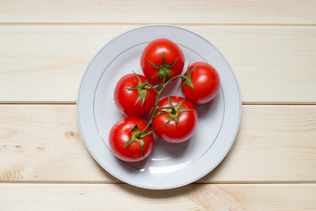 Ripe cherry tomatoes on branch laid on plate on light wooden background. Water drops on washed vegetables. Top view. Close-up. Central location. Raw foods. Healthy breakfast concept.の写真素材