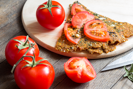 Healthy homemade snack for a vegan diet. Preparation of raw sandwich from dehydrated crisp bread and tomatoes. Fresh vegetables and knife on wooden table. Selective focus in the middle. Close-up.の写真素材