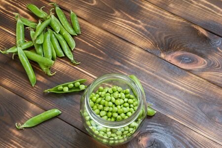 Fresh green peas in glass jar and whole pods on dark wooden table. Top angle view background with copy space. Place for text. Natural organic home-grown food concept. Raw diet. Healthy nutrition.の写真素材