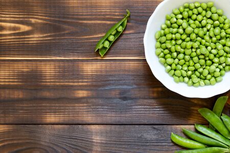Healthy organic food concept with copy space. Fresh delicious green peas peeled in white plate and whole pods on dark wooden table. Top view. Place for text. Natural nutrition. Raw diet. Vegan menu.の写真素材