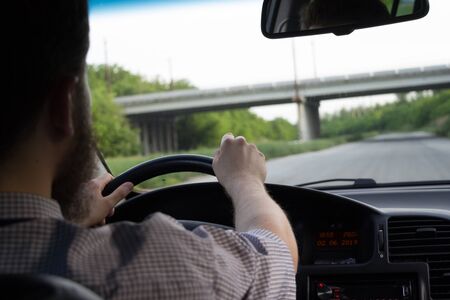 Young bearded man in summer shirt driving a car on highway. Both hands holding a steering wheel. Safe driving concept. Vの写真素材
