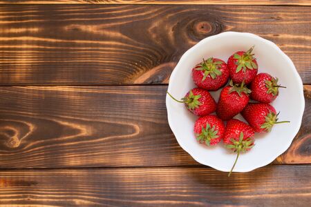 Juicy red strawberries in white bowl on wooden background with copy space at left side. Top view. Close-up. Delicious dessert. Summer harvest. Yummy natural organic food. Healthy meal.の写真素材