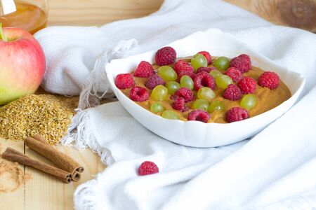 Vegan flax porridge with raspberry and grape raisins in white bowl on linen fabric. Raw food diet breakfast.の写真素材