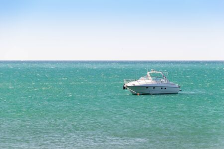 White boat anchored in a turquoise water of sea bay. Skyline and clear sky in frame. Vacation at...