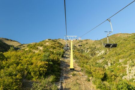 Chairlift to top of hill of mountain with blue sky in background. Sightseeing concept. Excursions at...