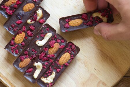 Men hand take healthy homemade chocolate sticks with almonds, cashews and raspberries, lie on a...