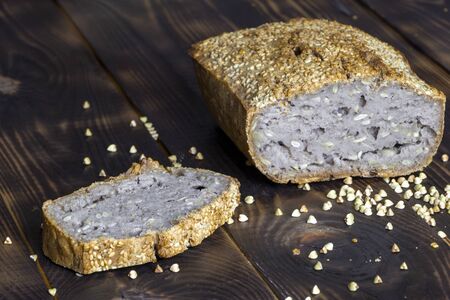 Vegan buckwheat bread. Freshly baked traditional bread on dark brown wooden table. Scattered grains...