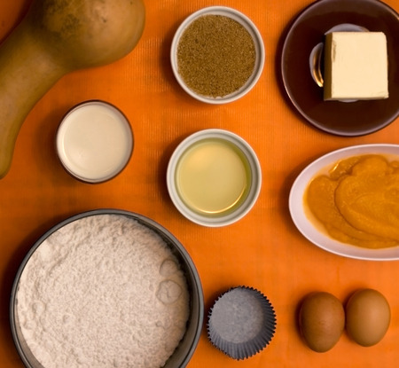 Food ingredients on orange background including pumpkin, brown sugar, flour, milk, oil, butter, mashed pumpkin and eggs.の写真素材