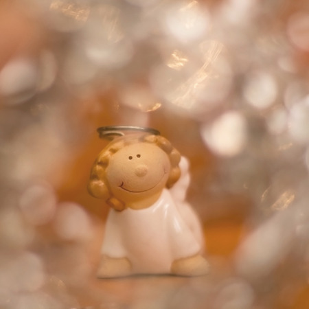 Little angel figurine, with orange background and Christmas bokeh. Selective focus.の写真素材