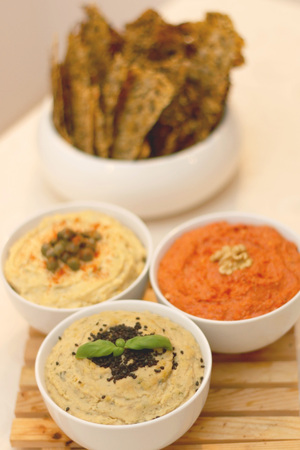 Three bowls with different dips: tuna dip, red pepper dip and hummus dip. Defocused crackers in the...