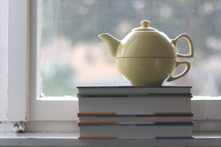 Teapot and pile of old books on rustic window. Selective focus.の写真素材