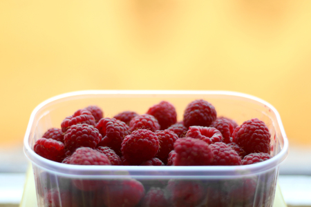 Raspberries in a transparent bowl. Bright yellow background, selective focus.