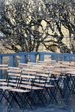 Rows of wooden chairs outdoor in public place. Decorative Christmas lights in the background, selective focus. In Zagreb, Croatia.の写真素材