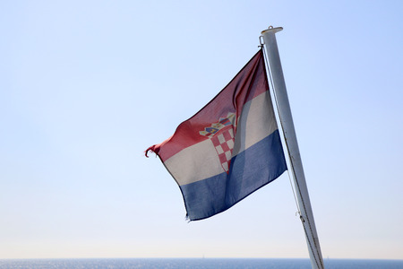 Croatian flag on a boat, blowing in the wind. Beautiful coast in the background. Selective focus.の写真素材