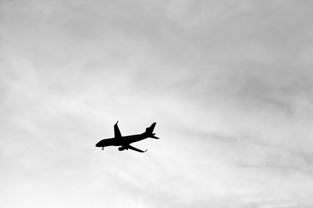 Plane silhouette on a cloudy sky, in black and white.
