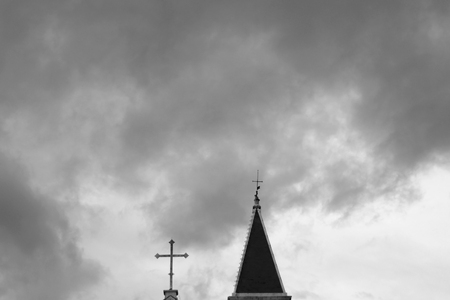 Church bell roof and cross with cloudy dark sky. Eery atmosphere. Copy space, black and white.の写真素材