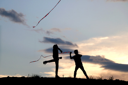 Two unrecognizable boys playing with ribbons in nature. Silhouettes of children with sunset sky in the background.の写真素材