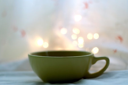 Cup of hot tea. Book and fairy lights in the background. Seletive focus.