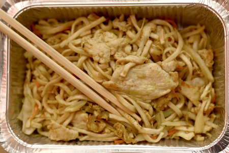 Noodles with chicken and vegetables in a metallic container with chopsticks. Top view, selective focus.の写真素材