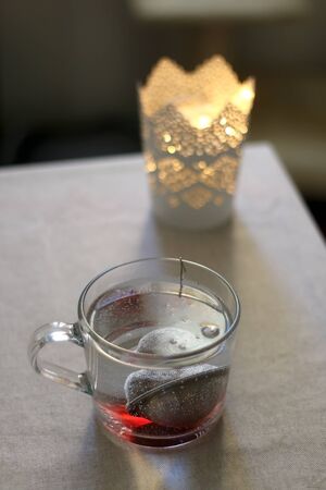 Cup of hot water with tea infuser. Candle holder in the background. Selective focus.の写真素材