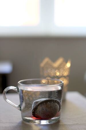 Cup of hot water with tea infuser. Candle holder in the background. Selective focus.の写真素材
