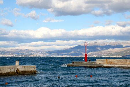 Small red lighthouse on the pier in Sutivan, island Brac, Croatia. Windy and cloudy weather, beautiful landscape.の写真素材