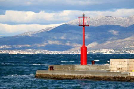 Small red lighthouse on the pier in Sutivan, island Brac, Croatia. Windy and cloudy weather, beautiful landscape.の写真素材