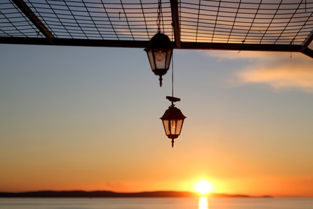 Silhouete of retro lanterns outdoor during beautiful sunset over the sea.の写真素材