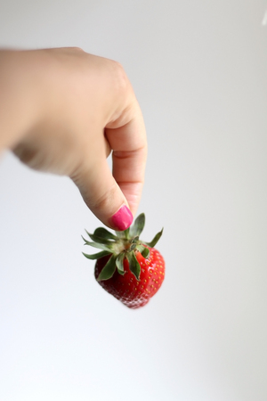 Unrecognizable person holding a strawberry. Selective focus, white background.の写真素材