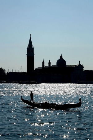 Silhouette of gondola and gondolier on a sunny day, in Venice, Italy. View of San Giorgio Maggiore church and island in the background.の写真素材