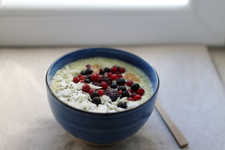 Fruit and vegetable smoothie (spinach, apple, banana, orange) with wild berries, chia seeds and coconut flake topping. Selective focus.の写真素材