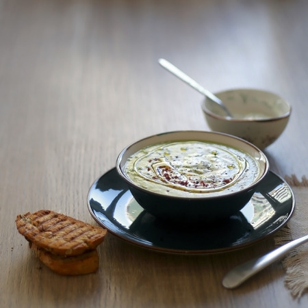 Creamy vegetable soup with kale, cabbage, celery and millet, decorated with olive oil, yoghurt sauce and chilli flakes. Served with toasted bread and lemony yoghurt sauce. Selective focus.の写真素材