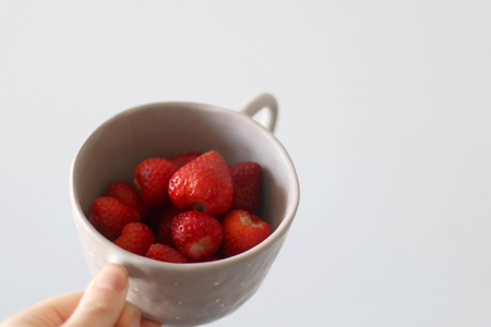Unrecognizable person holding a bowl of strawberries. Selective focus, white background.の写真素材