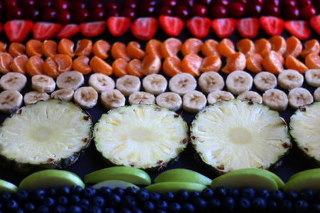 Various fruit arranged in rainbow colors: cherries, strawberries, tangerines, banana, pineapples, apples and blueberries. Selective focus.の写真素材