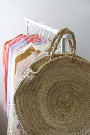 Colorful vintage wardrobe on a clothes rack. Fashionable straw bag in the front. Selective focus.の写真素材