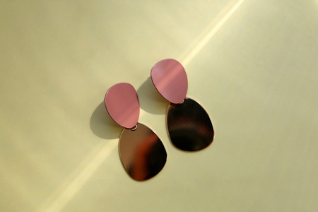 Fashionable golden earrings on yellow background, illuminated by sunlight.