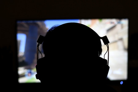Silhouette of unrecognizable man with headset playing game in front of screen. Selective focus.の写真素材