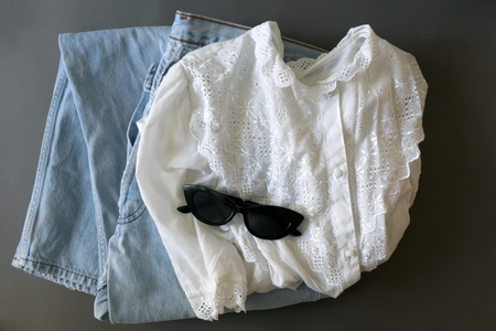 Fashionable outfit with vintage white blouse and washed out jeans. Flat lay, gray background.の写真素材